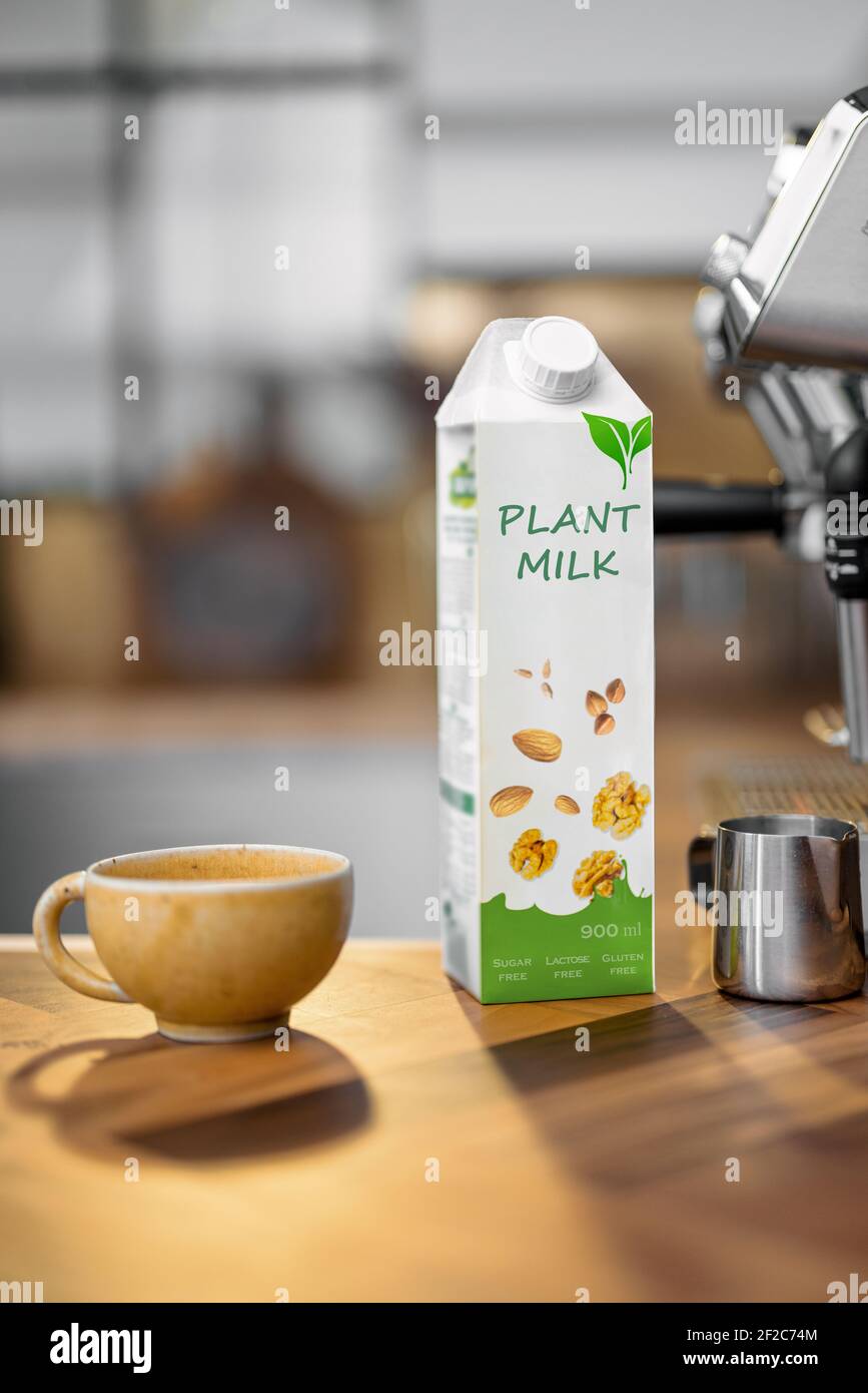 Confezionamento di latte vegetale vicino ad una tazza di caffè e macchina da caffè su un tavolo di legno in cucina. Latticini biologici, bevanda alternativa. Foto Stock