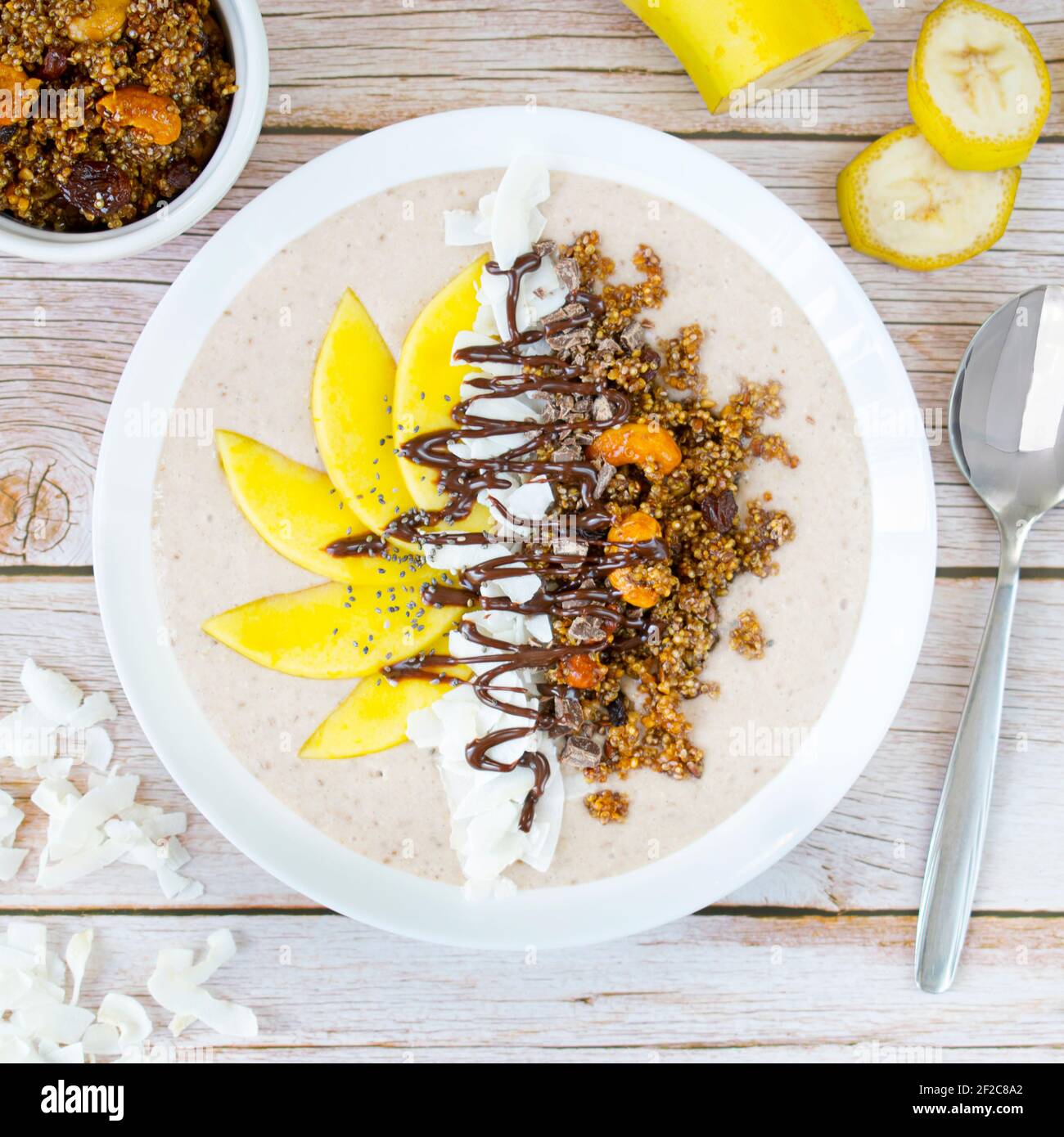 Ciotola di cocco-banana con granola di quinoa e frutta fresca di mango. Foto Stock