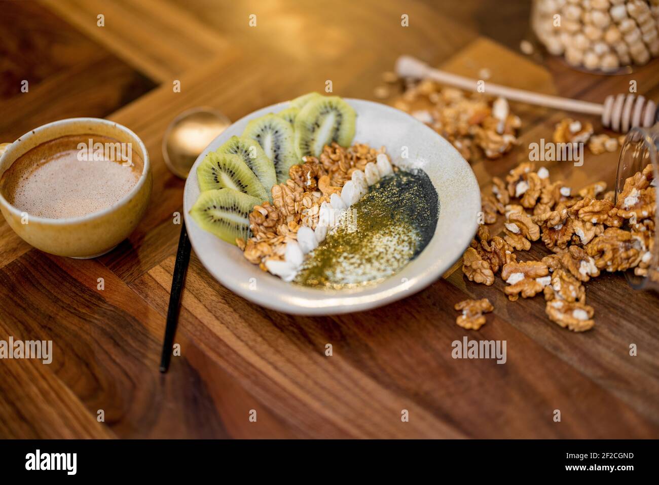 Colazione sana con ciotola di granola con kiwi, spirulina e yogurt biologico su tavolo di legno in cucina con noci e caffè sullo sfondo. Foto Stock