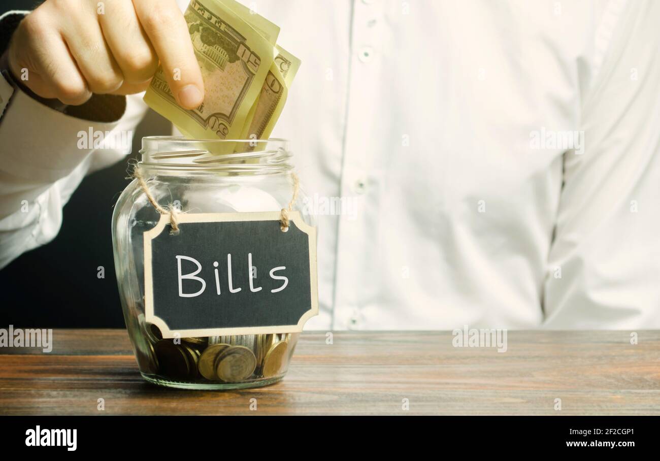 Un uomo mette i soldi in un vaso di vetro con la parola Bills. Concetto di pagamento della bolletta di servizio. Alloggio, elettricità, bollette dell'acqua. Conto, affari e finanza. S Foto Stock
