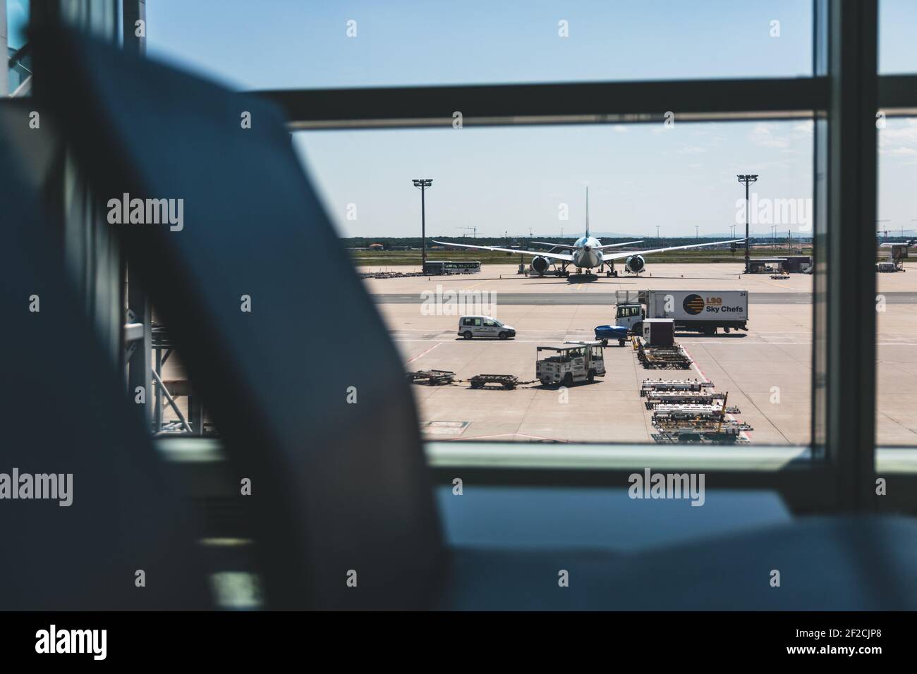 Una calda giornata all'aeroporto. Un solo aereo è in piedi fuori al sole. Sono visibili diversi veicoli. Fotografato attraverso una finestra. Foto Stock