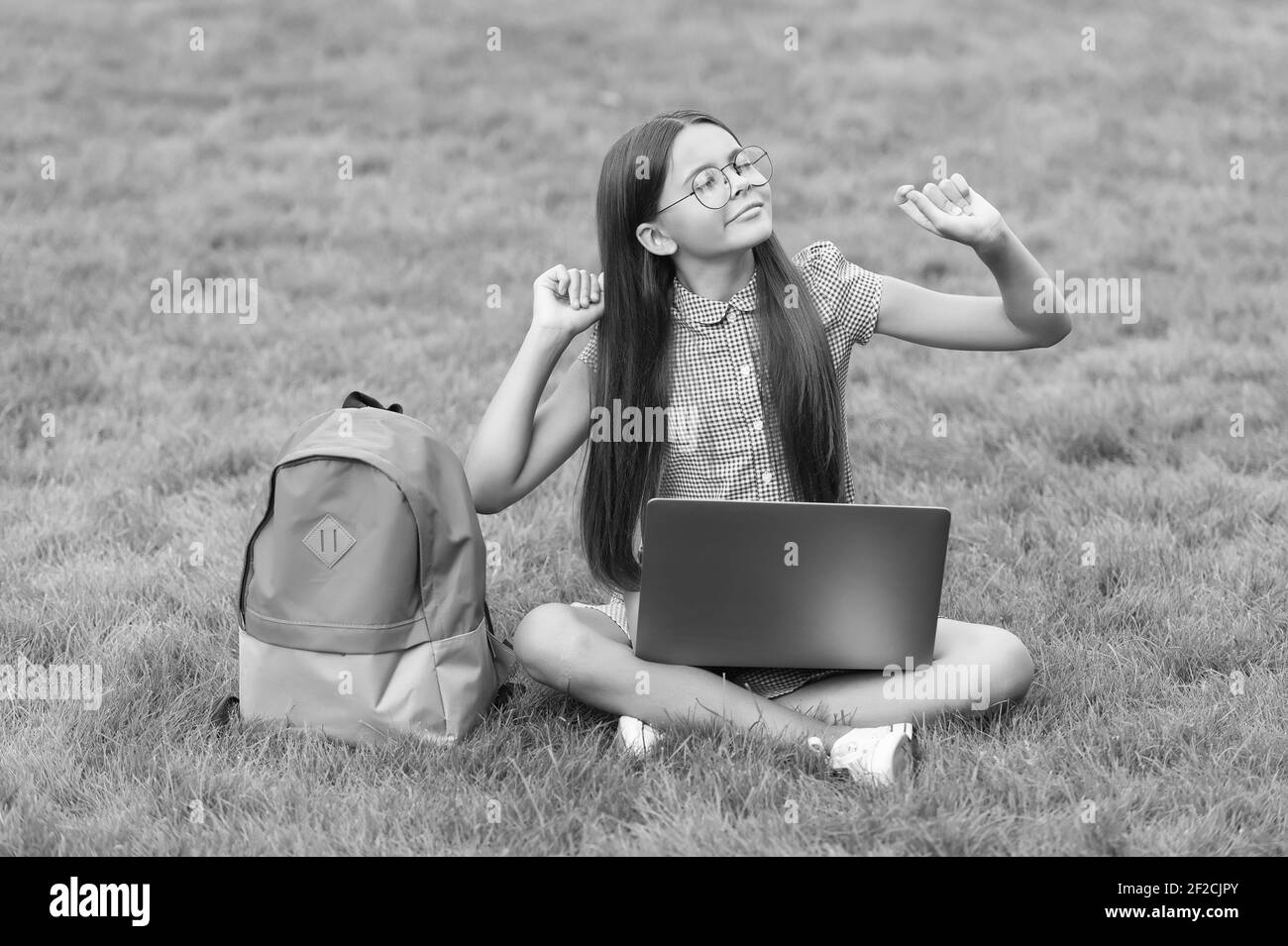 Tempo libero. Ritorno a scuola. Formazione online. Giorno della conoscenza. Lezione privata per bambini. Blogging. Ragazza spensierata seduta su erba verde con laptop. Avvio. Bambino che gioca al computer. Foto Stock