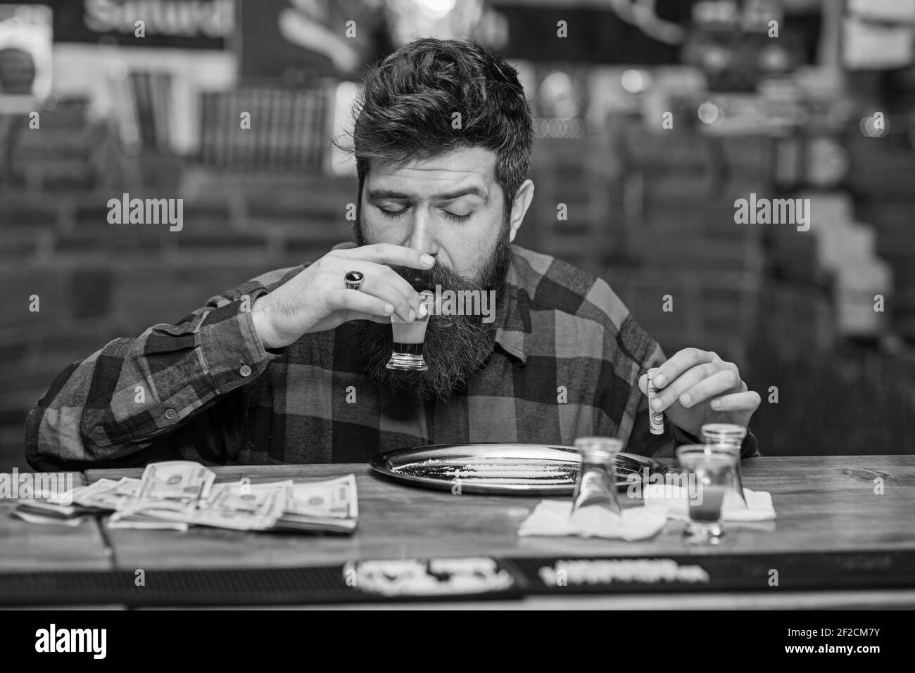 Guy passare il tempo libero al bar ottenendo alto, sfondo sfocato. Uomo con il viso ubriaco e allegro, siediti da solo al bancone del bar. L'hipster contiene un cocktail e un tubo per la sniffing delle droghe. Concetto di divertimento illegale. Foto Stock