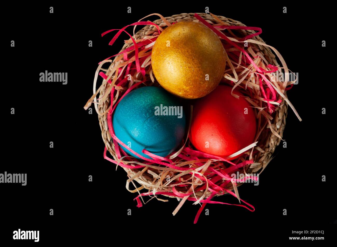 Uova di Pasqua dipinte in casa multicolore su paglia multicolore in un cesto di vimini su sfondo scuro, isolamento Foto Stock
