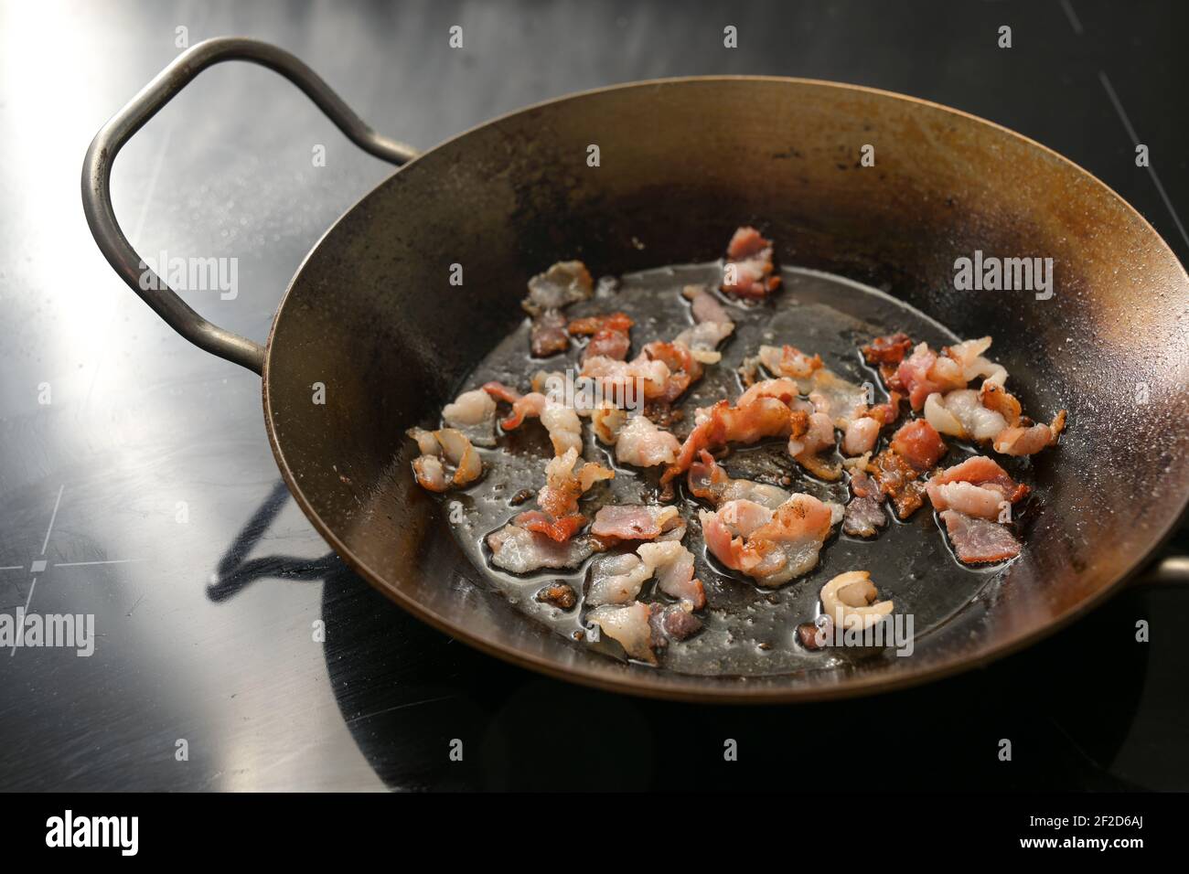 Pezzi croccanti tritati di pancetta fritti in una padella di ferro sulla stufa nera, spazio di copia, fuoco selezionato, profondità di campo stretta Foto Stock