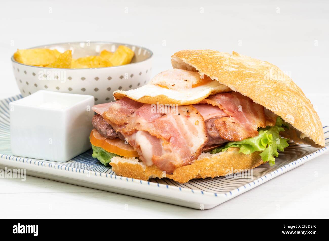 Hamburger speciale con pancetta e uova fritte, patatine fritte e salsa mayo Foto Stock