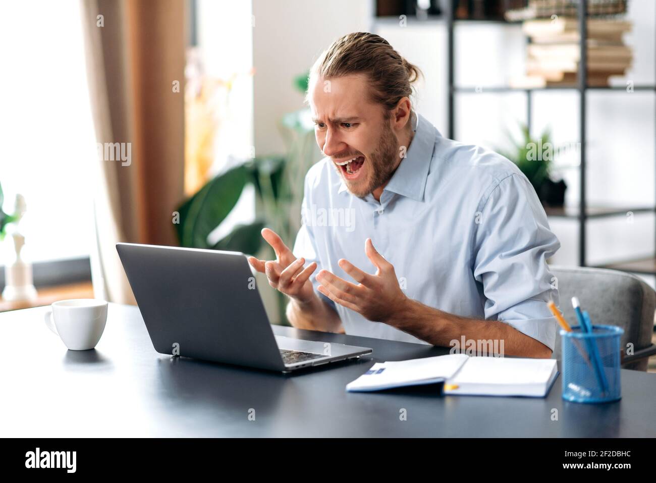 Infastidito caucasico busy business guy che guarda un portatile in confusione, ha ricevuto notizie inaspettate, ha fallito un accordo, grida, gesturing con le mani, seduto alla scrivania dell'ufficio di casa Foto Stock