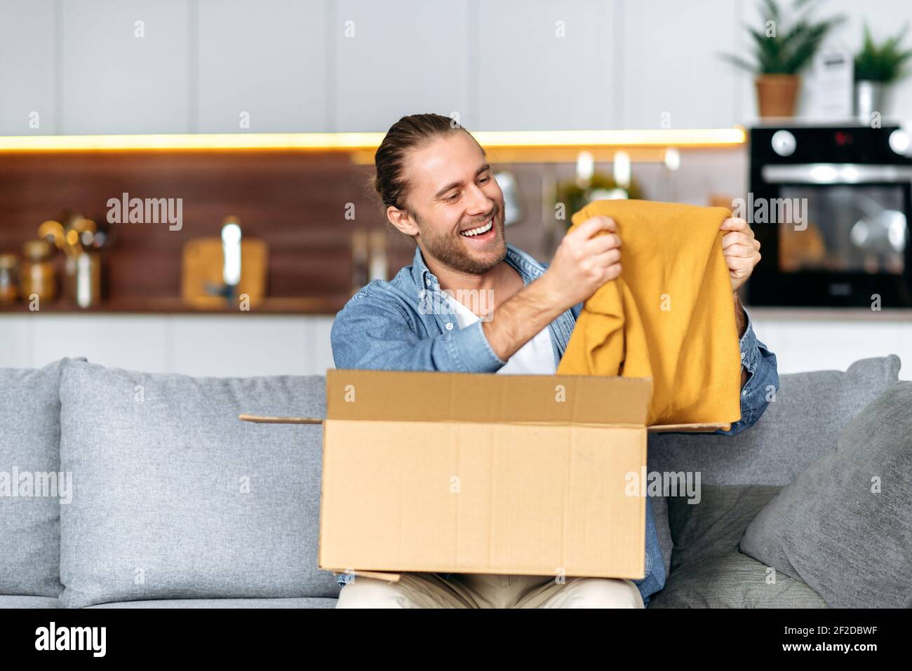 Sorridente attraente uomo disimballato il suo pacco, felice circa ottenere  un lungo ordine previsto. Caucasico ragazzo