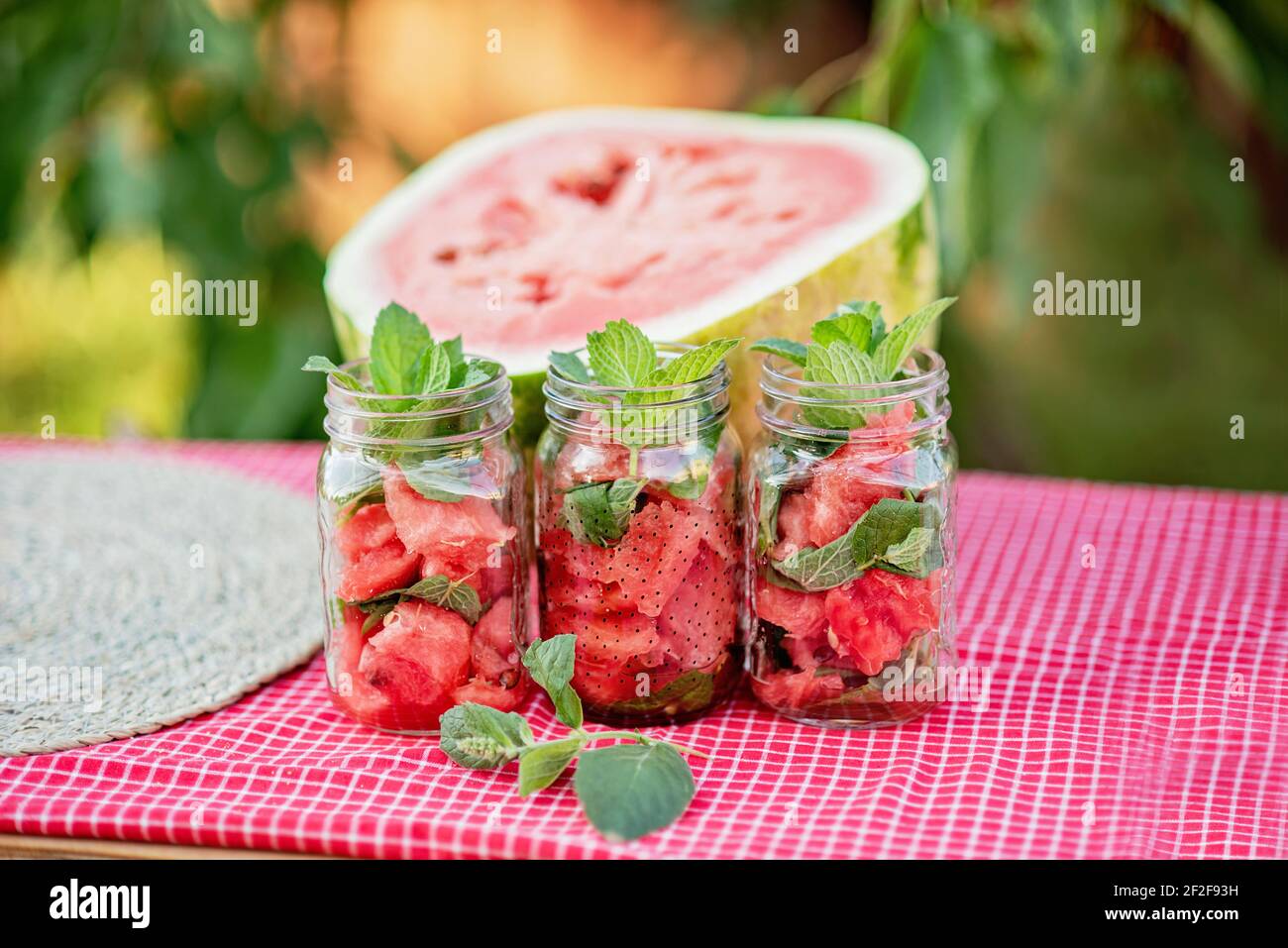 Anguria e menta infusarono acqua detox. Limonata con ghiaccio e menta come rinfrescante bevanda estiva in vasi. Bevande analcoliche fredde con frutta. Rinfrescante su rosso Foto Stock