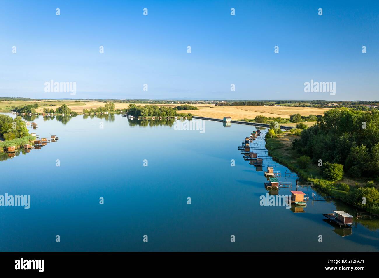 La calma superficie del lago riflette il cielo senza nuvole. Case di palafitte dei pescatori intorno alle banche. Estate sera in natura. Foto Stock