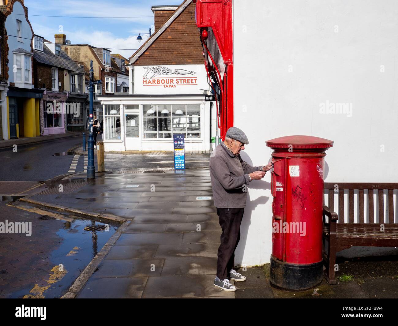 Un uomo anziano in un cappello piano che postava una lettera nel centro di Whitstable. Foto Stock