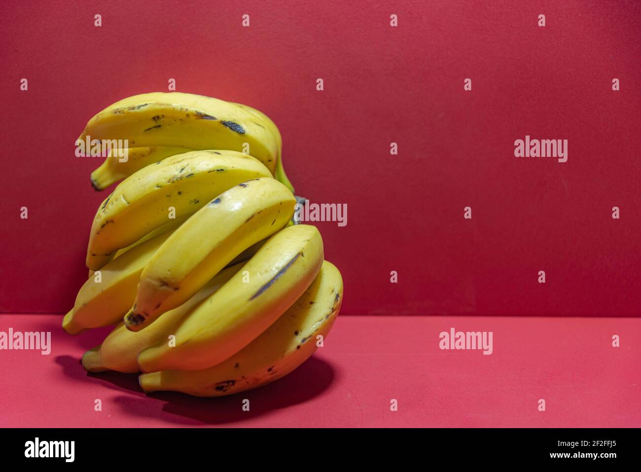 Mazzo di banane gialle. Banane su sfondo rosso. Frutta esotica ricca di fibra e fonte di potassio. Banana frutta (Musa spp.). Pianta tipica di Foto Stock