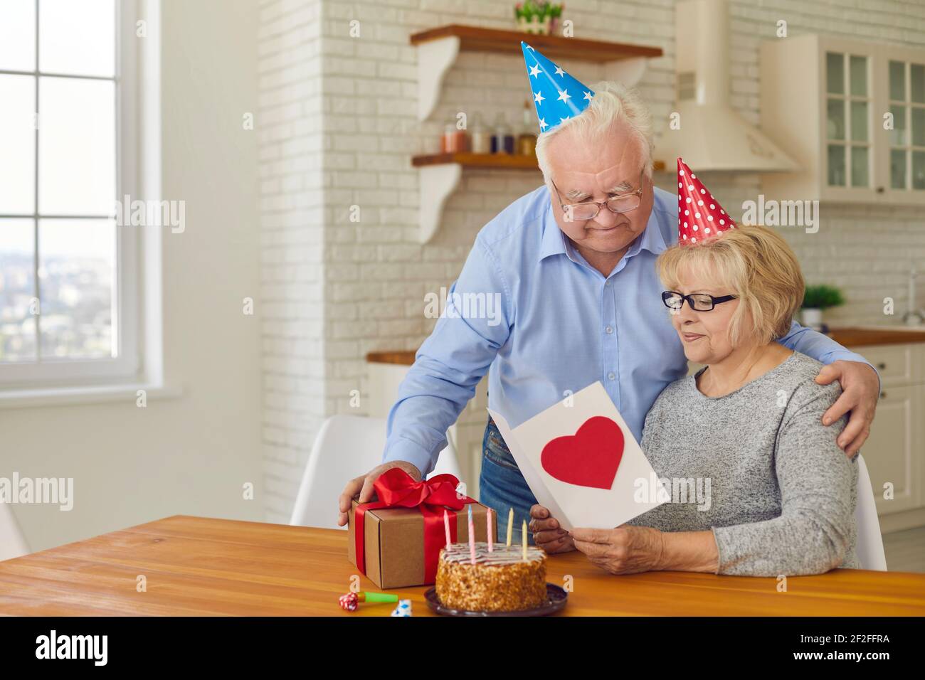 Il marito più anziano si congratula con sua moglie per il suo compleanno, dando la sua torta, regalo e biglietto di auguri Foto Stock