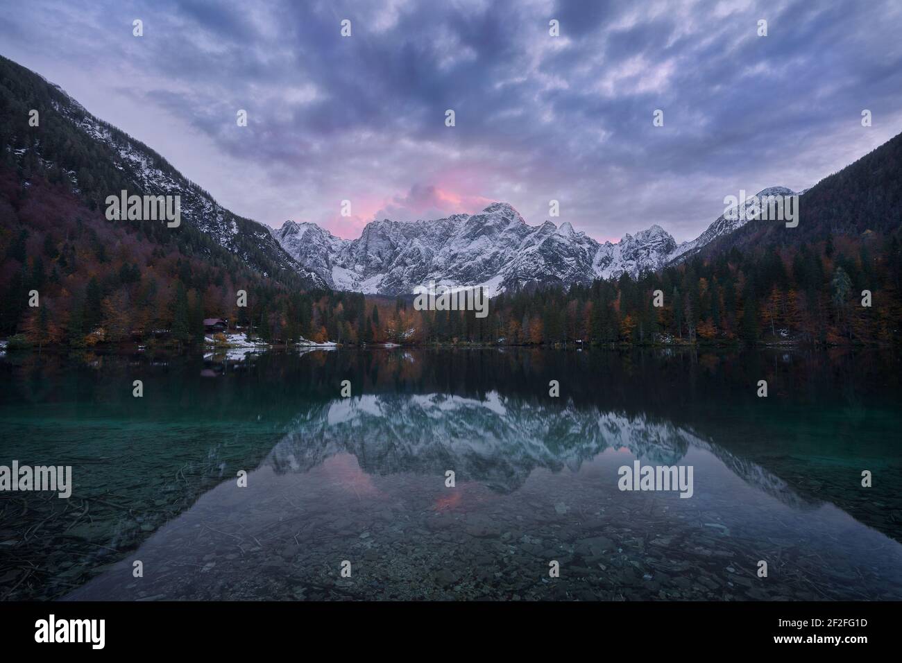 Tramonto sul lago inferiore Fusine durante la stagione delle foglie con neve picchi sullo sfondo e un bel riflesso nel acqua cristallina Foto Stock