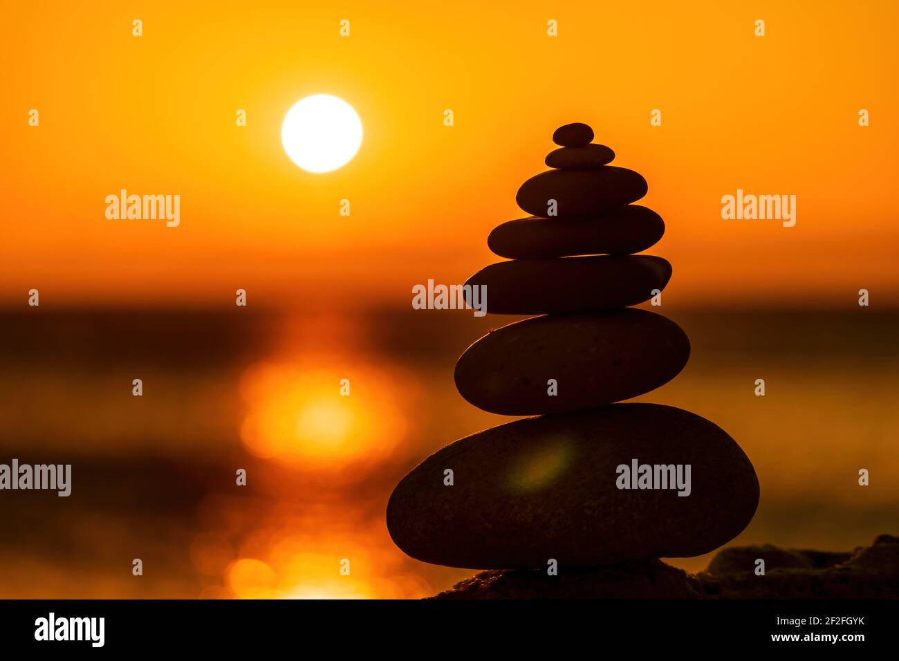 Profilo a piramide di ciottoli bilanciato sulla spiaggia. Astratto caldo tramonto bokeh con Mare sullo sfondo. Pietre Zen sulla spiaggia di mare, meditazione, spa Foto Stock
