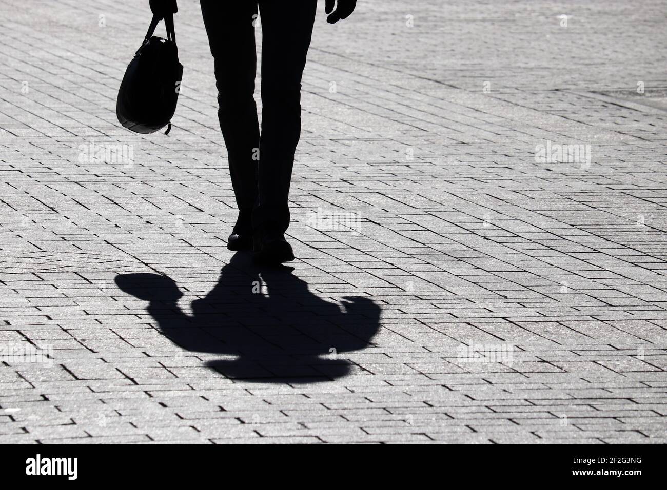Silhouette nera di uomo sottile con valigia che cammina per strada, ombra su un marciapiede. Concetto di uomo d'affari, avanzamento di carriera Foto Stock