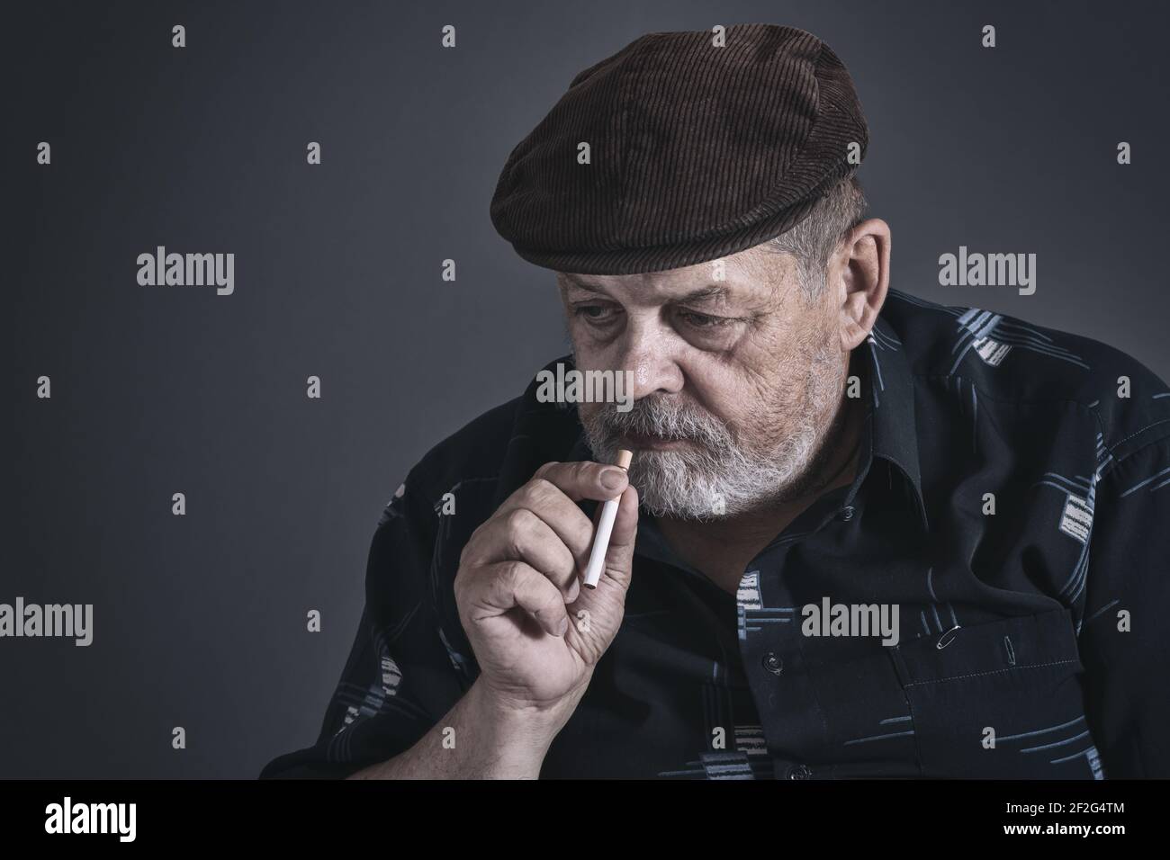 Drammatico ritratto basso chiave di esitante anziano caucasico con sigaretta Foto Stock