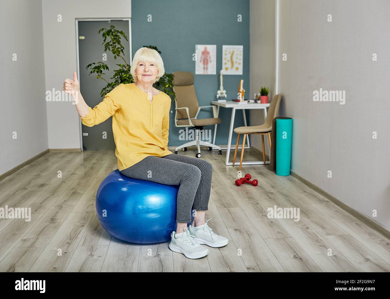 Donna anziana che mostra i pollici in su mentre addestrando ad un wellness centro Foto Stock