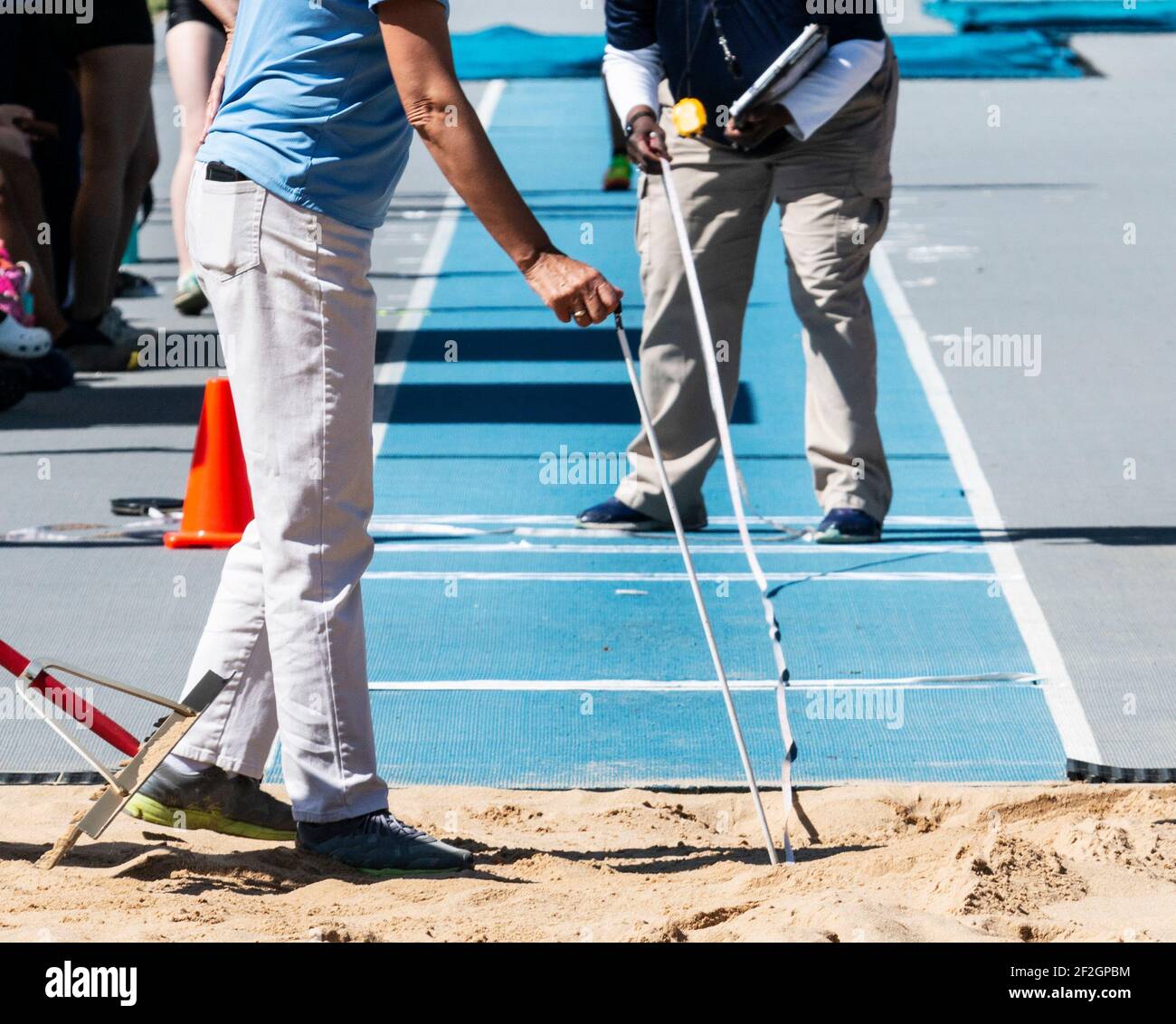 I funzionari di pista che misurano la distanza di un salto degli atleti nella buca di sabbia con una pista blu all'aperto. Foto Stock