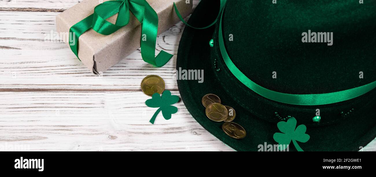 Cappello Leprechaun, monete d'oro, trifoglio shamrock e regalo con nastro verde su sfondo bianco. Simboli di buona fortuna per il giorno di San Patrizio. Vacanza irlandese. BA Foto Stock