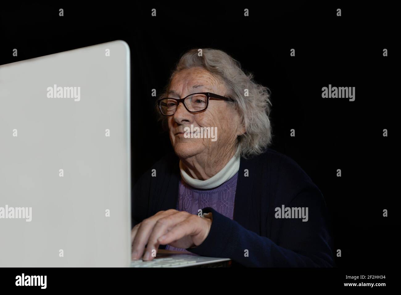 Donna anziana felice che usa il laptop a casa su sfondo scuro.Lifestyle ritratto maturo 80 s femmina con nuova tecnologia shopping online, video di famiglia chiama Foto Stock