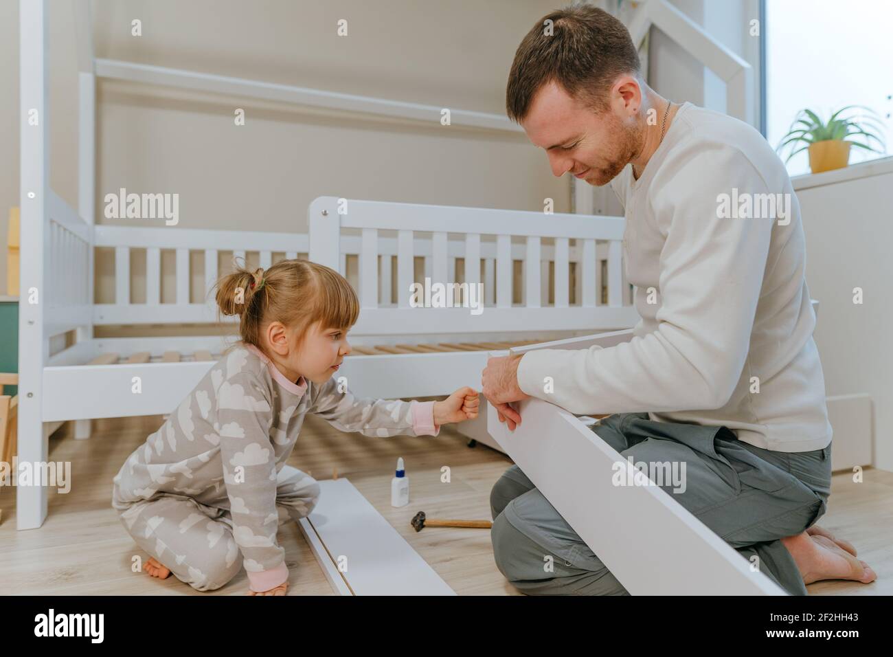 Bambina di 4 anni aiuta suo padre a assemblare o fissare il cassetto di letto nella camera da letto dei bambini. Foto Stock
