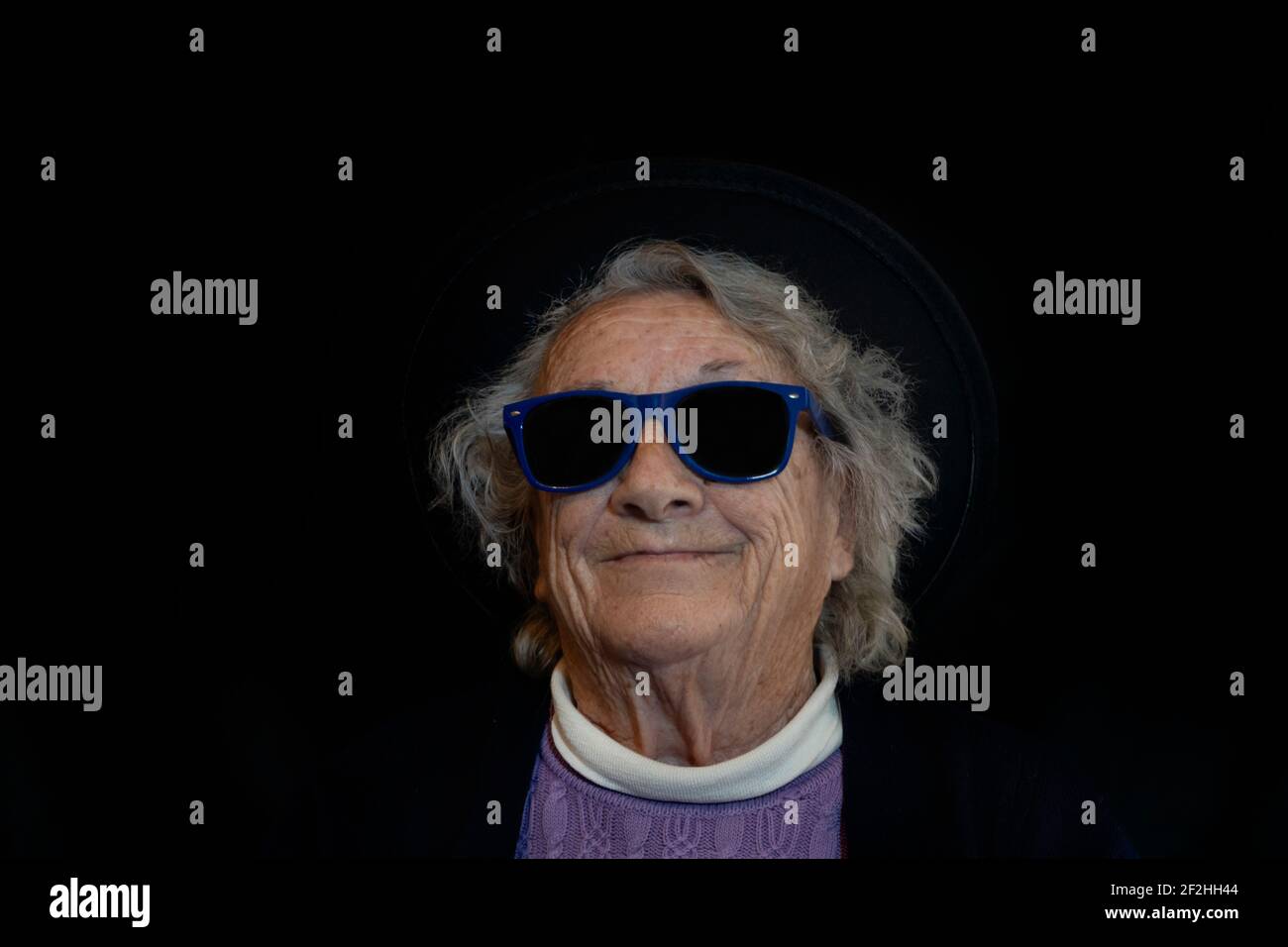 Anziano anziano 80s donna con occhiali da sole su sfondo scuro.Ritratto persone anziane che hanno divertimento, studio stile di vita concetto. Foto Stock