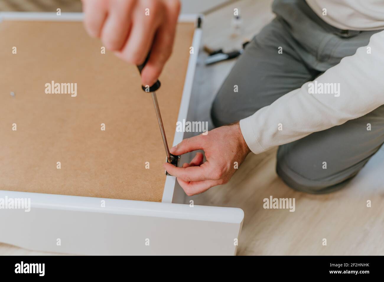 Primo piano delle mani maschio ruotando la vite con un cacciavite in una scatola di legno di letto per bambini Foto Stock