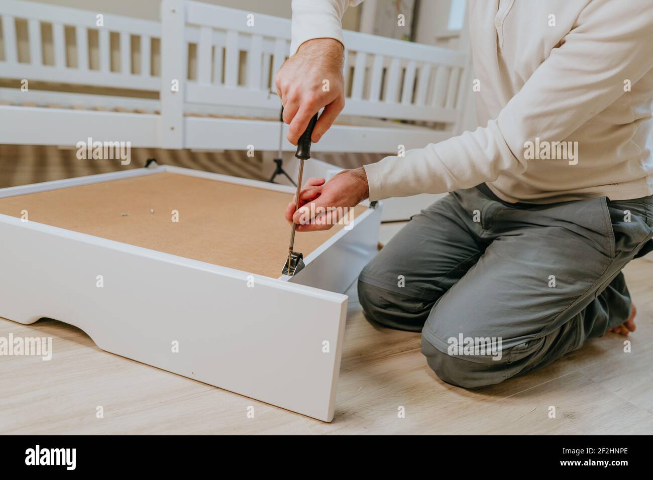 Primo piano delle mani maschio ruotando la vite con un cacciavite in una scatola di legno di letto per bambini Foto Stock
