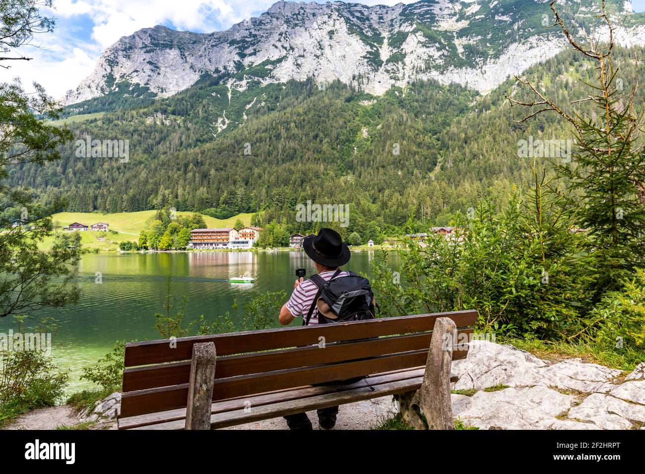 L'escursionista siede su una panchina e filma il paesaggio con la piccola macchina fotografica, Hintersee, Ramsau, nella parte posteriore Reiteralpe, Berchtesgaden, Alpi Berchtesgaden, Parco Nazionale Berchtesgaden, Berchtesgadener Land, Alta Baviera, Baviera, Germania, Europa Foto Stock