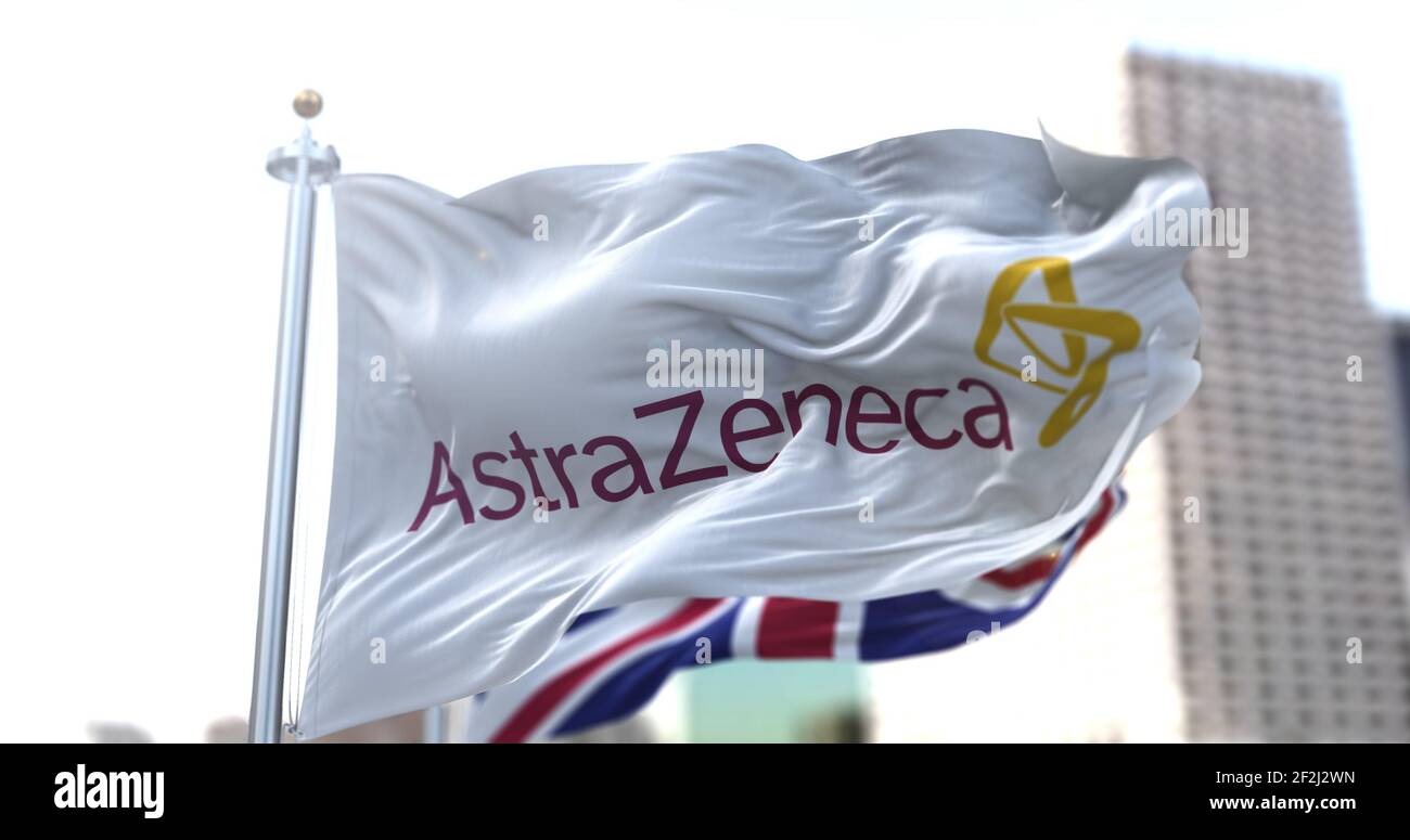 Londra, UK, 28 gennaio 2021: Bandiera bianca con il logo AstraZeneca che sventola nel vento e bandiera inglese sullo sfondo. Foto Stock