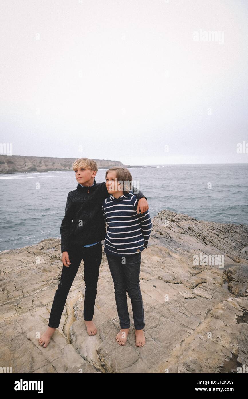 I migliori amici posano a piedi nudi su una scogliera rocciosa vicino a. oceano Foto Stock