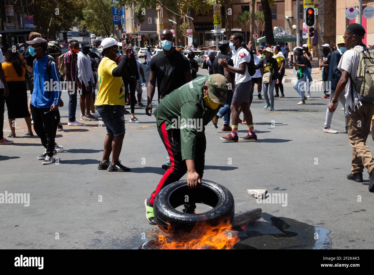 Un protettore che ha posto un pneumatico dell'automobile sul fuoco durante la manifestazione.gli allievi protestano contro il rifiuto dall'università di wits registrare gli allievi con gli arretrati delle tasse di iscrizione. Foto Stock