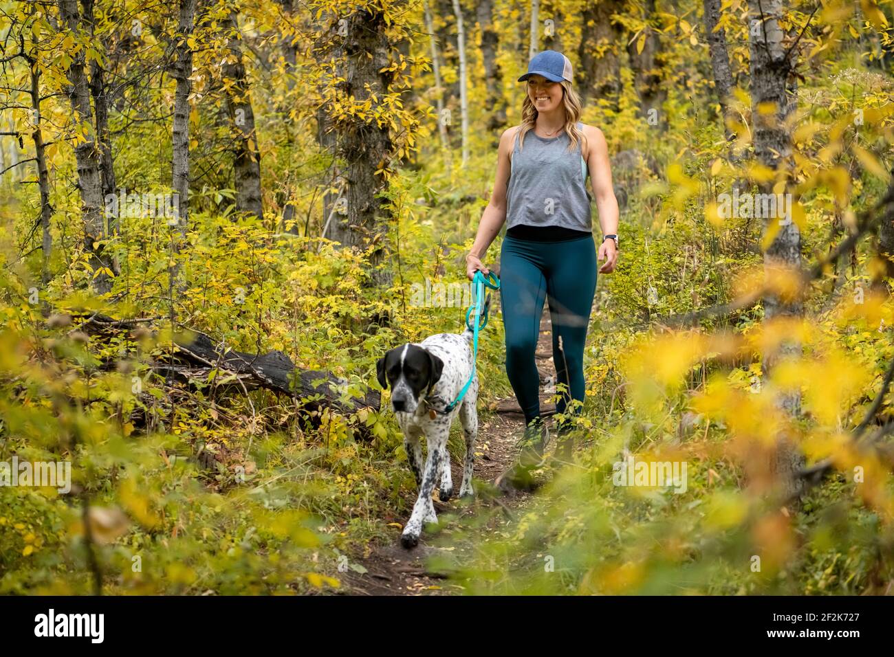 Sorridente giovane donna che cammina con il cane tra piante autunnali in foresta Foto Stock