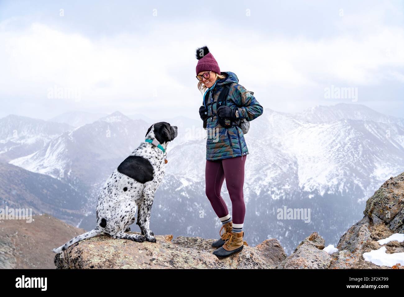 Giovane donna sorridente con cane puntatore sulla cima di montagna mentre escursioni durante le vacanze Foto Stock
