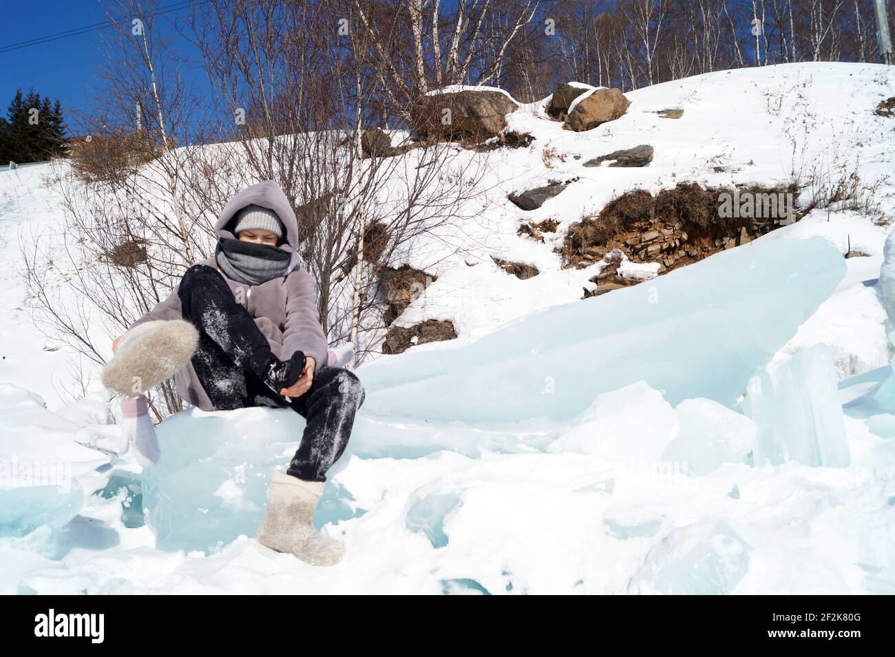 Una ragazza di 10-15 anni si siede su un ghiaccio galleggia e scuote la neve ou Foto Stock