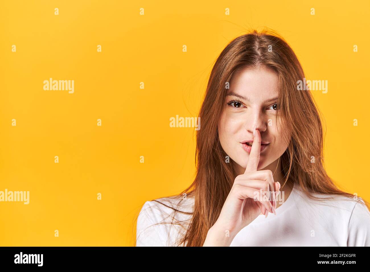 Ritratto giovane ragazza, mostrando silenzio con le labbra che toccano le dita. Isolato su sfondo giallo brillante Foto Stock