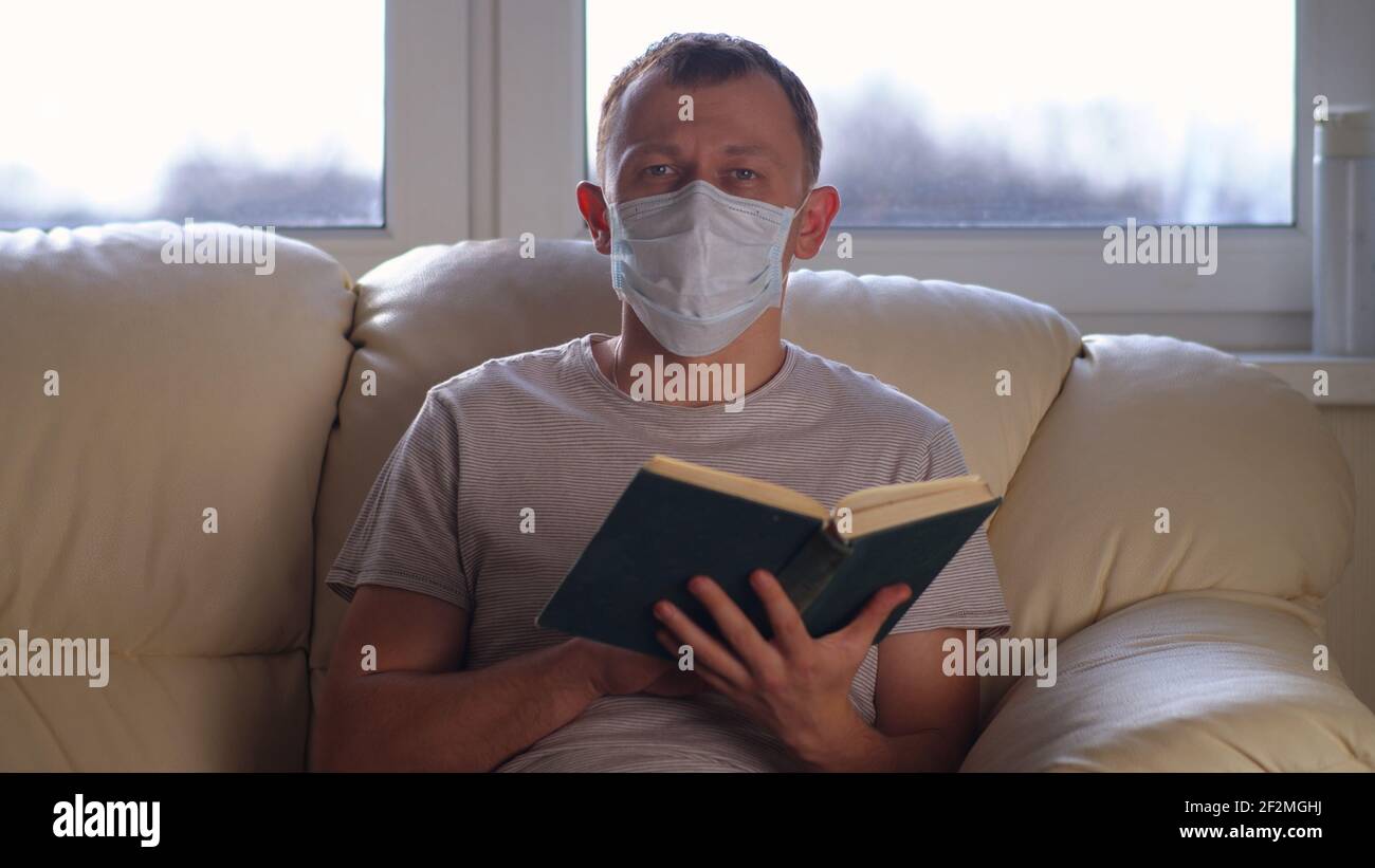 Giovane uomo a casa sul divano leggere un libro, auto-isolamento, sfondo finestra Foto Stock