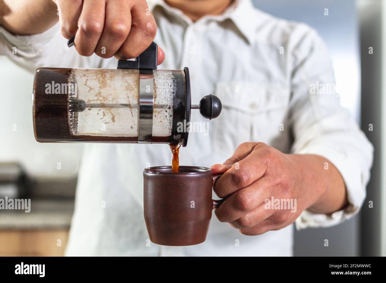 Le mani dell'uomo servono il caffè in una tazza da una pressa francese. Messa a fuoco selettiva Foto Stock