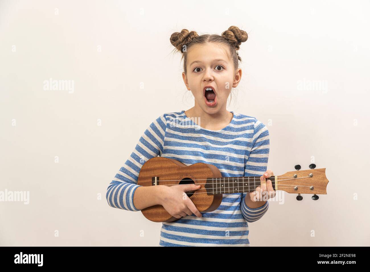 La ragazza canta e suona l'ukulele. Il bambino ride, si pone per la macchina fotografica e gode la musica. Imparare a giocare ukuleles. Foto Stock