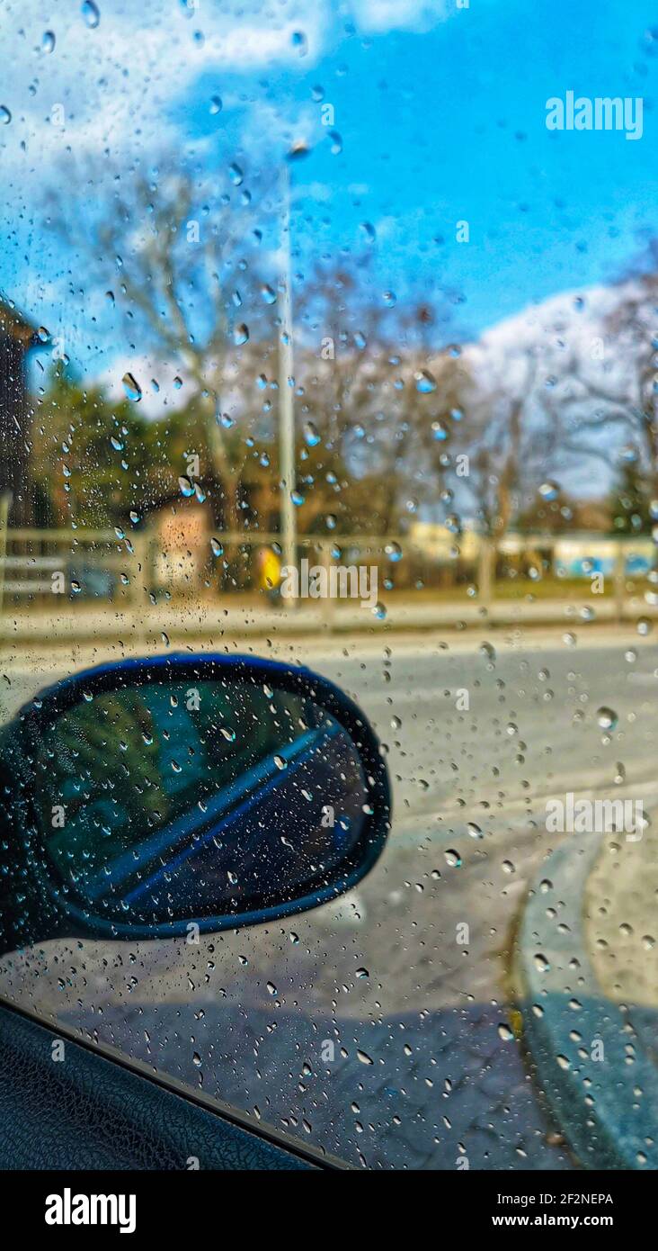 Gocce d'acqua sul parabrezza di un'auto in giornata di sole. Vista sulla strada attraverso il vetro del finestrino della vettura coperta da gocce di pioggia Foto Stock
