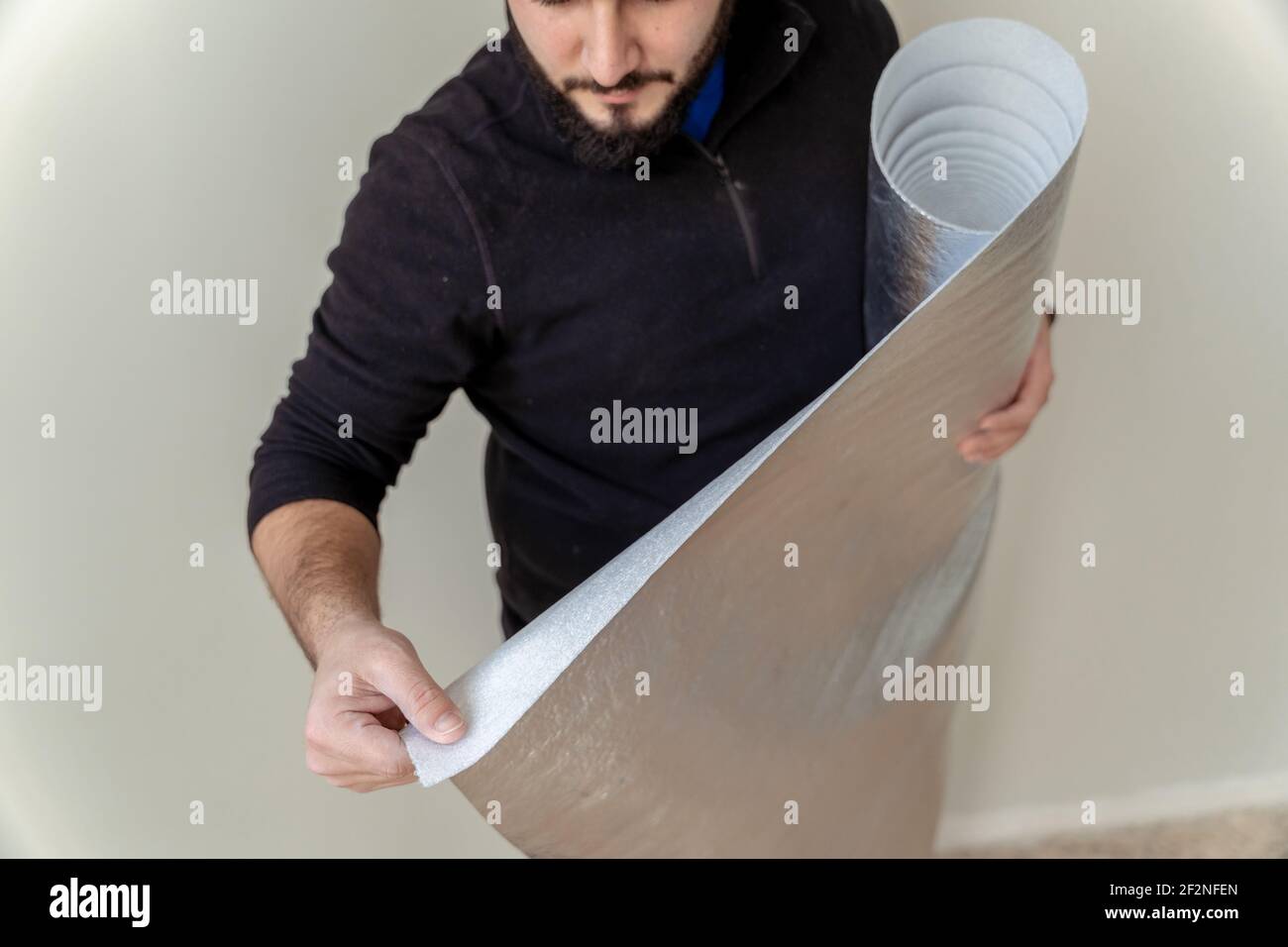 primo piano di un uomo utilizzando un rotolo di isolante panno per installare un pavimento in legno Foto Stock
