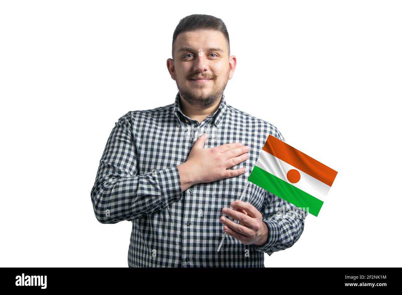 Ragazzo bianco che tiene una bandiera di Niger e tiene la mano sul suo cuore isolato su uno sfondo bianco con amore per Niger. Foto Stock