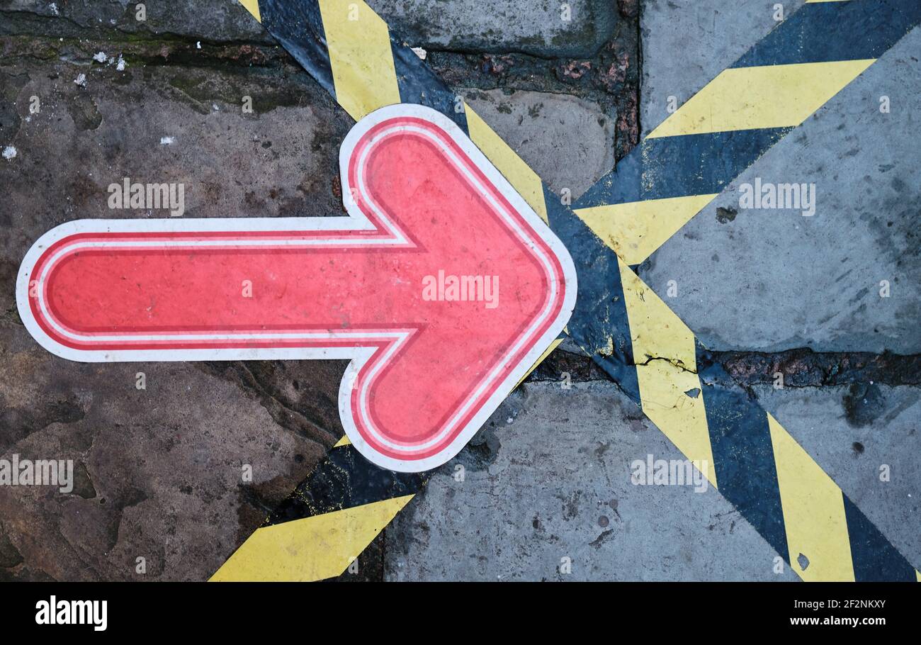 freccia rossa bloccata su un marciapiede, con nastro di avvertimento giallo e nero, che indica ai pedoni dove camminare Foto Stock