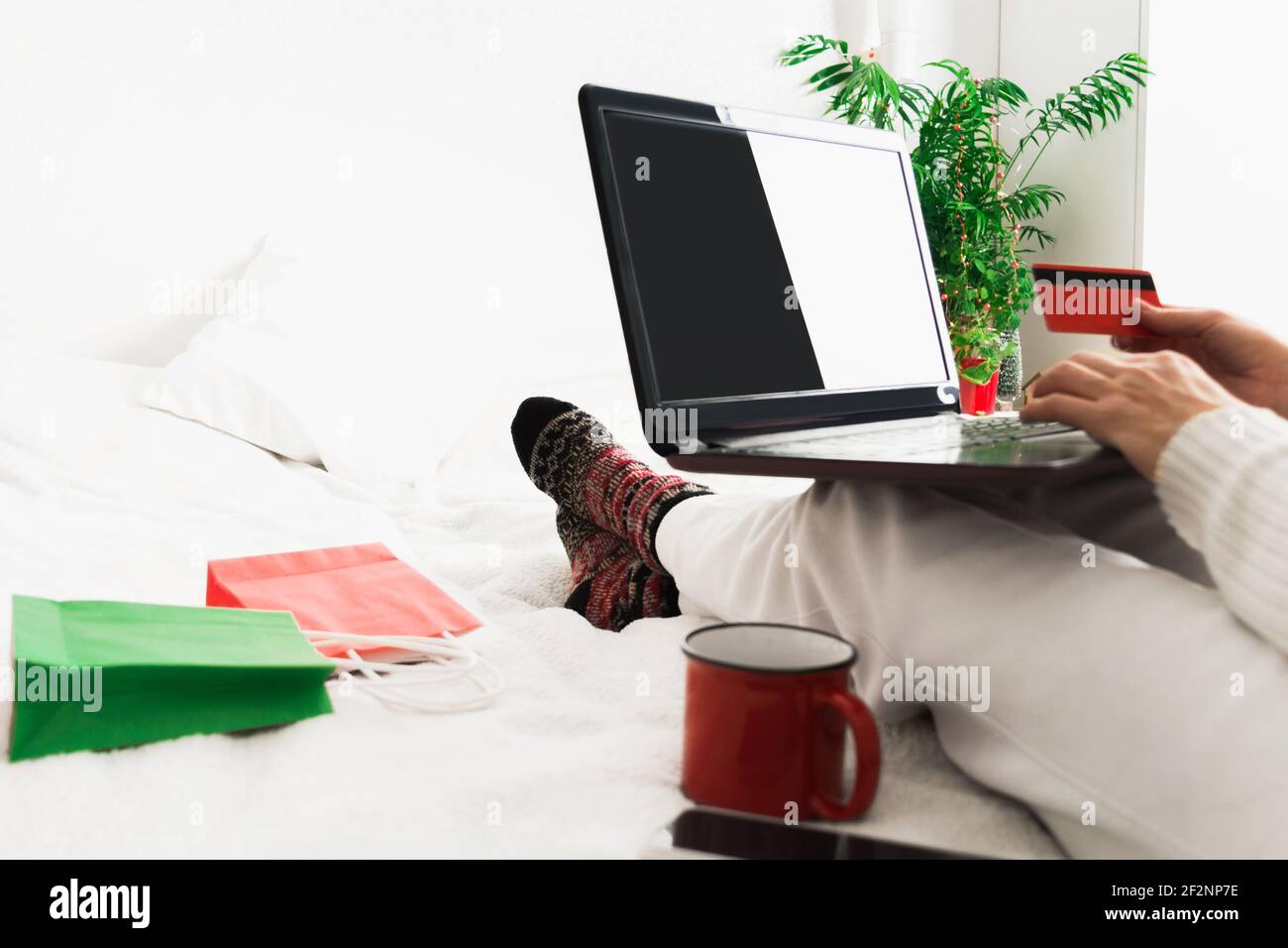 Giovane donna a casa con computer portatile, carta di credito rossa e tazza facendo shopping Foto Stock