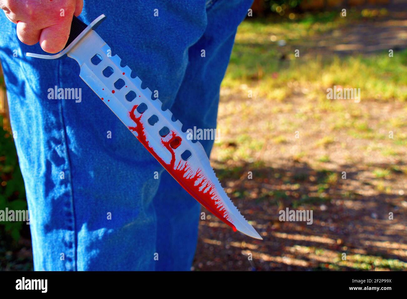 Un enorme coltello Bowie con sangue che scorre giù la lama in una mano maschile; crimine violento o concetto di terrorismo Foto Stock