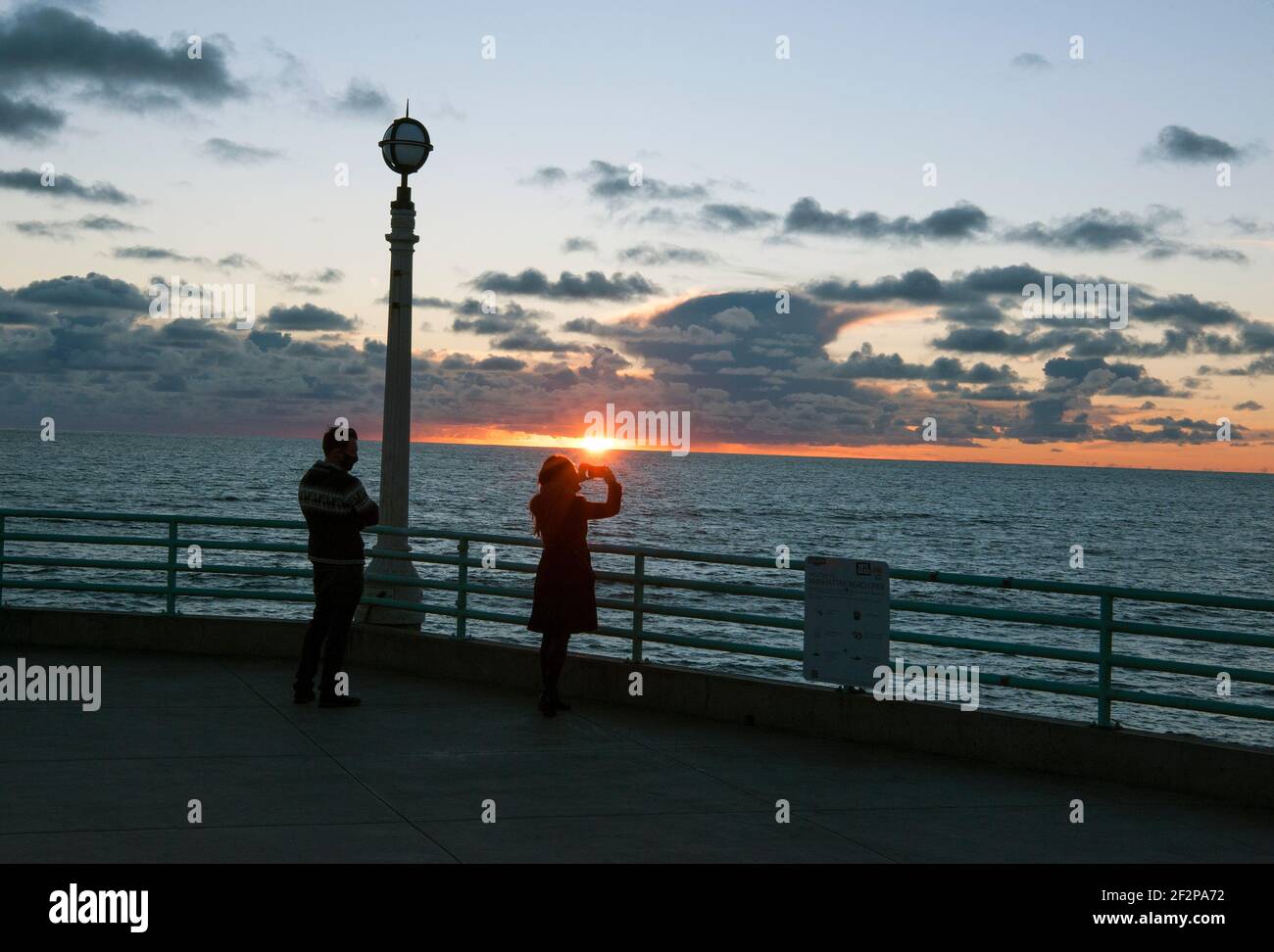 Una donna scatta una foto del tramonto dal molo di Manhattan Beach, California Foto Stock