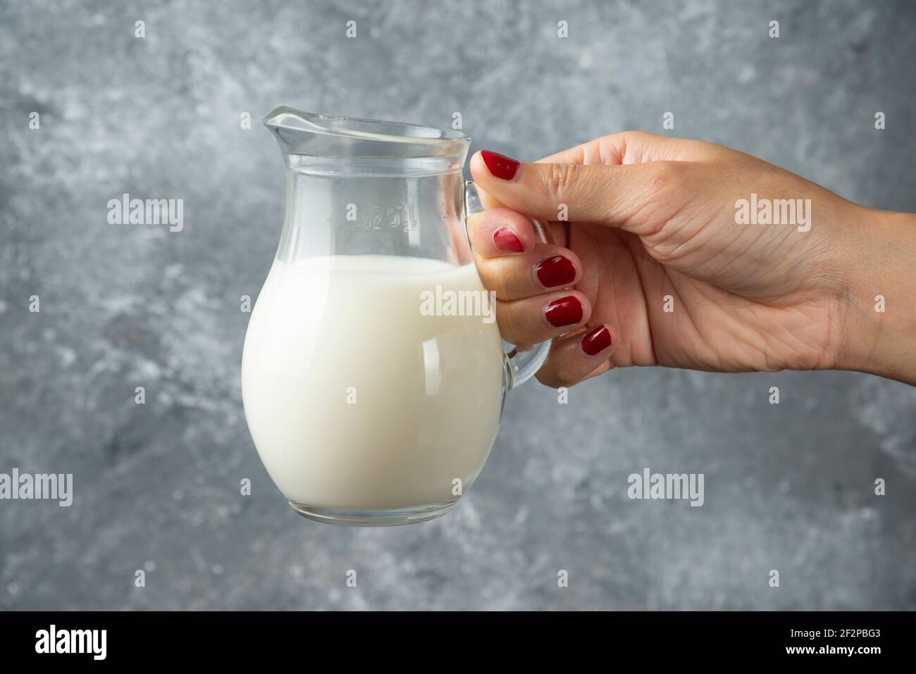 Donna mano che tiene vaso di vetro di latte su sfondo di marmo Foto Stock