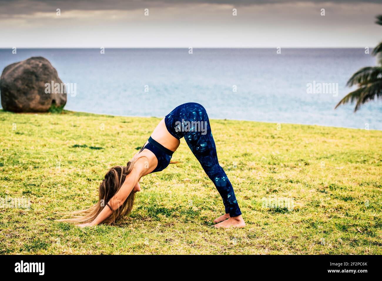Giovane donna in pilates esercitarsi nella posizione di idoneità sul verde campo nella natura - attività sportive all'aperto persone per stile di vita sano - vista oceano Foto Stock