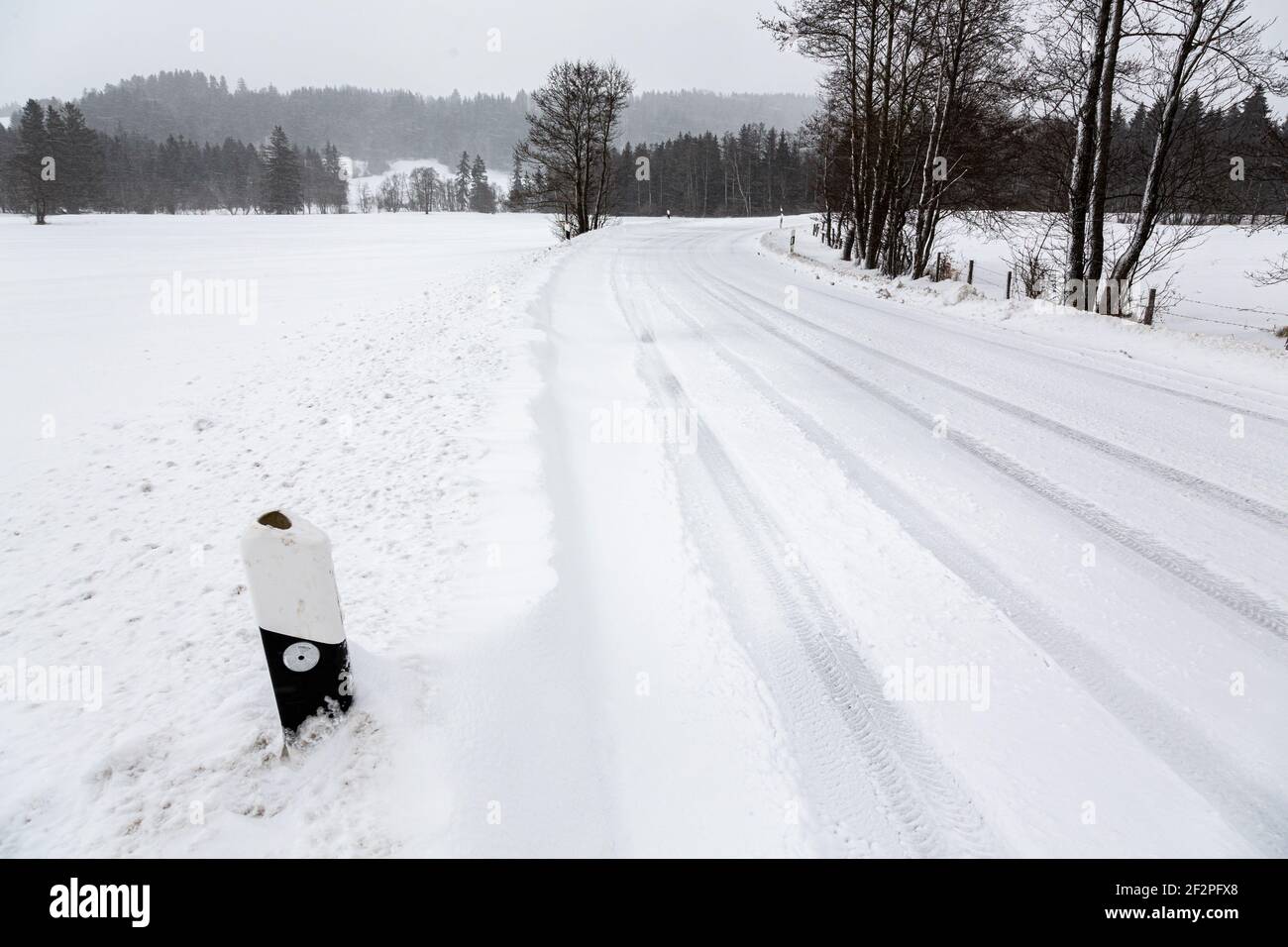 Germania, Baviera, strada di campagna innevata con piste per pneumatici e pali di delimitazione del traffico innevato. Foto Stock